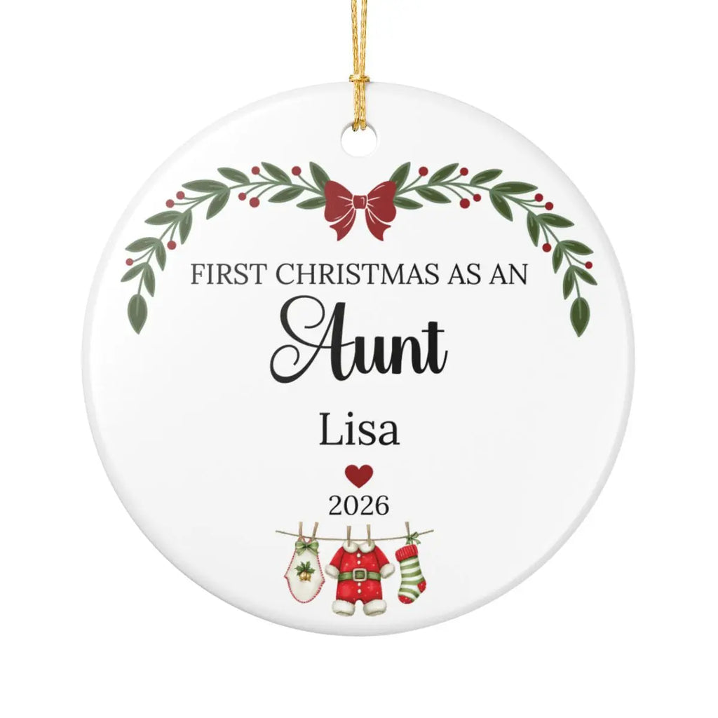 A round white personalized Christmas ornament with a gold hanging string. The ornament features printed black text reading 'FIRST CHRISTMAS AS AN Aunt' with the name 'Lisa' below, plus holiday illustrations including a green wreath with red berries, a red bow, a red heart, and Christmas stockings on a clothesline.