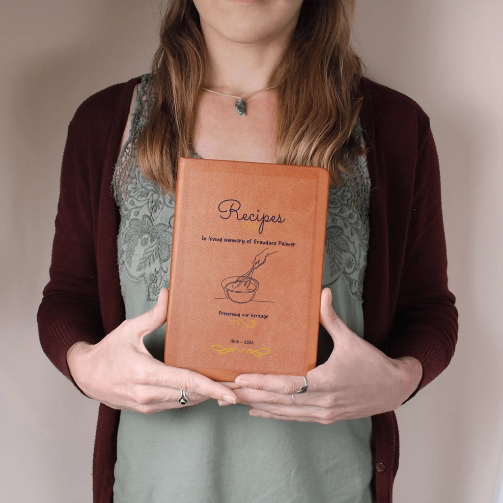 Person holding a leather-bound recipe book with text and illustrations on a plain background