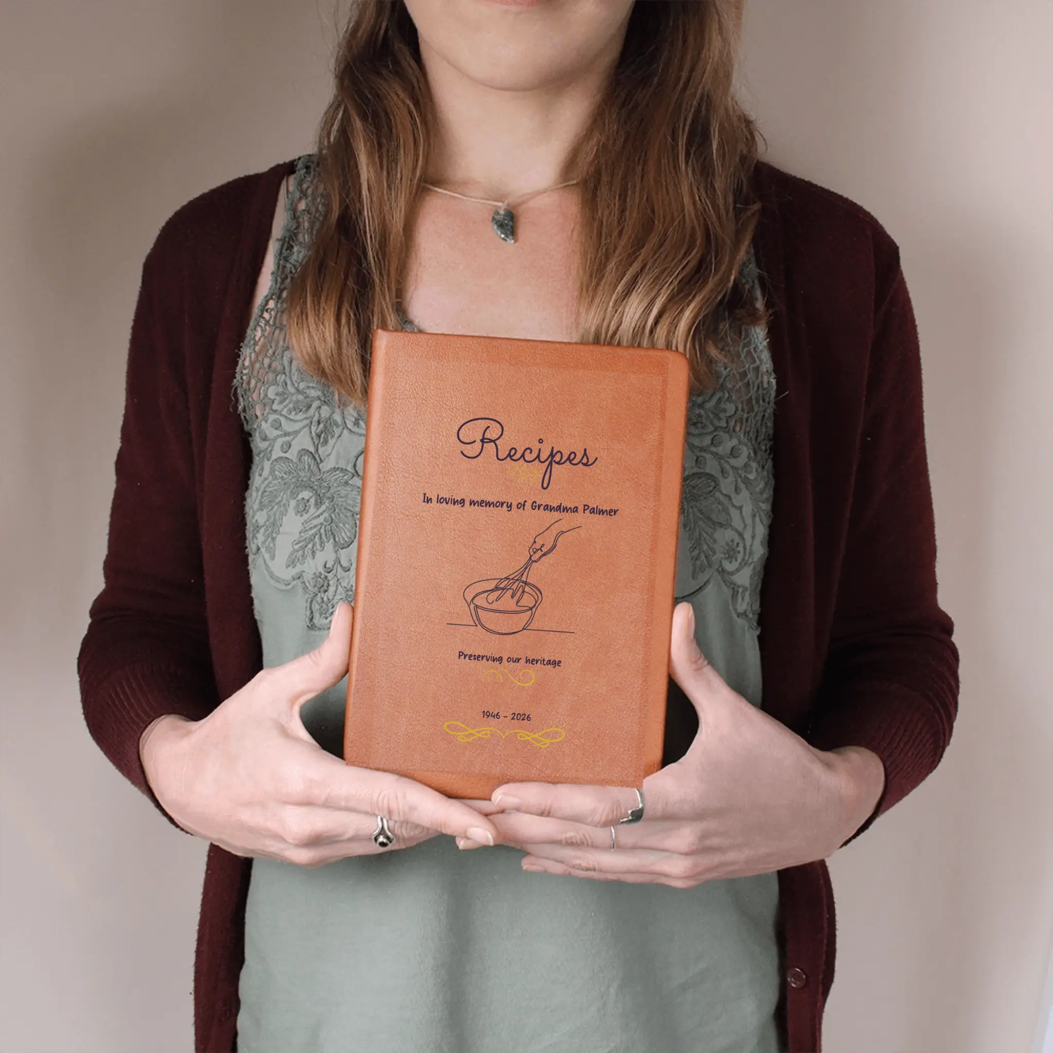 Person holding a leather-bound recipe book with text and illustrations on a plain background