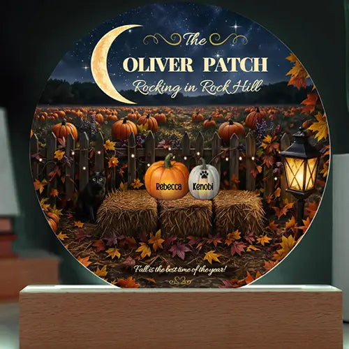 A round decorative plaque mounted on a wooden base, featuring a Halloween-themed autumn scene with pumpkins, fall leaves, a fence, a black cat, and a lantern. The plaque includes customizable text reading 'The Oliver Patch Rocking in Rock Hill' and names printed on pumpkin and dog-shaped decorations.
