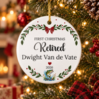 A personalized round ceramic Christmas ornament hanging from a decorated Christmas tree. The white ornament features the text 'FIRST CHRISTMAS Retired Dwight Van de Vate 2026' with green holly leaves, red berries, a red bow, and a small fish illustration at the bottom.