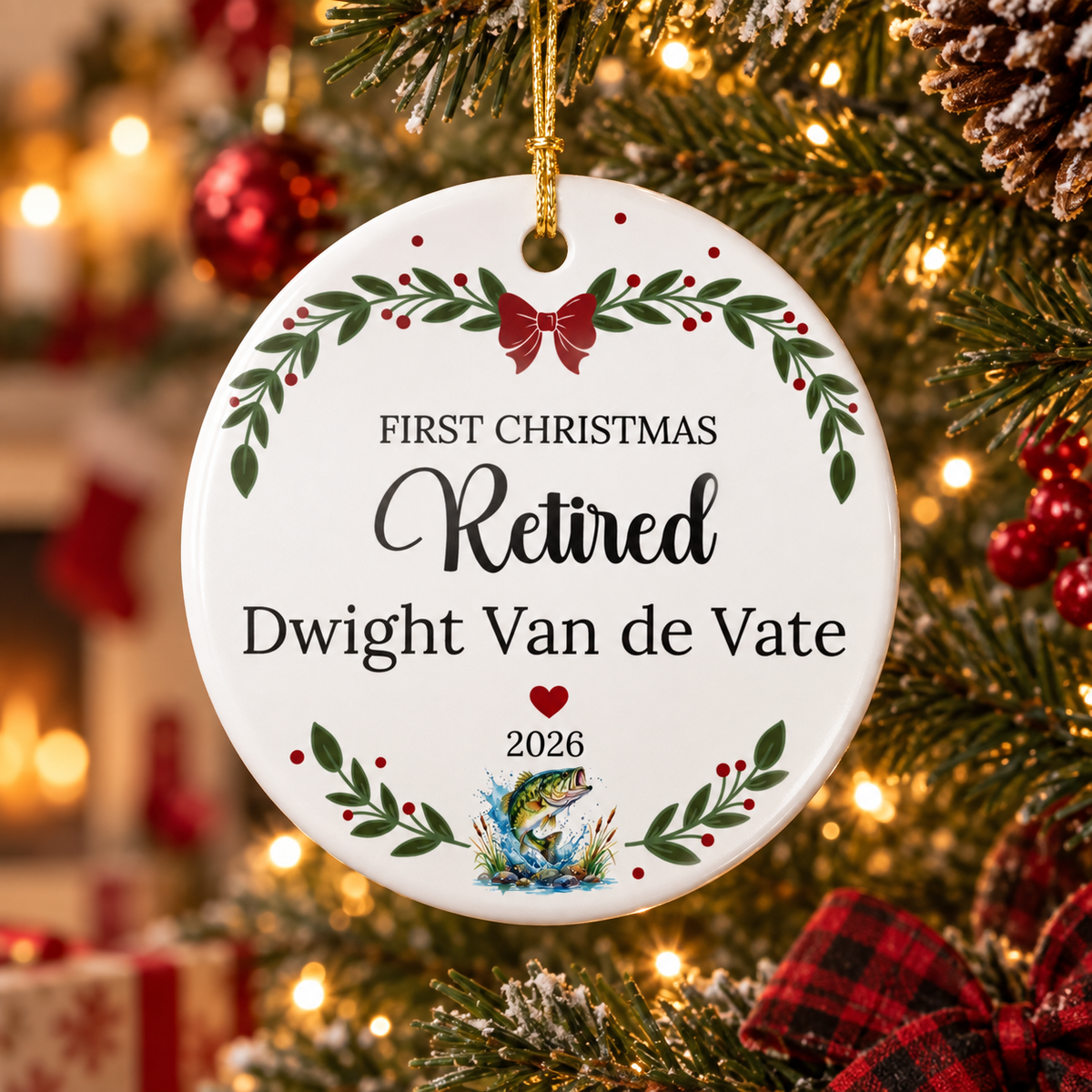 A personalized round ceramic Christmas ornament hanging from a decorated Christmas tree. The white ornament features the text 'FIRST CHRISTMAS Retired Dwight Van de Vate 2026' with green holly leaves, red berries, a red bow, and a small fish illustration at the bottom.