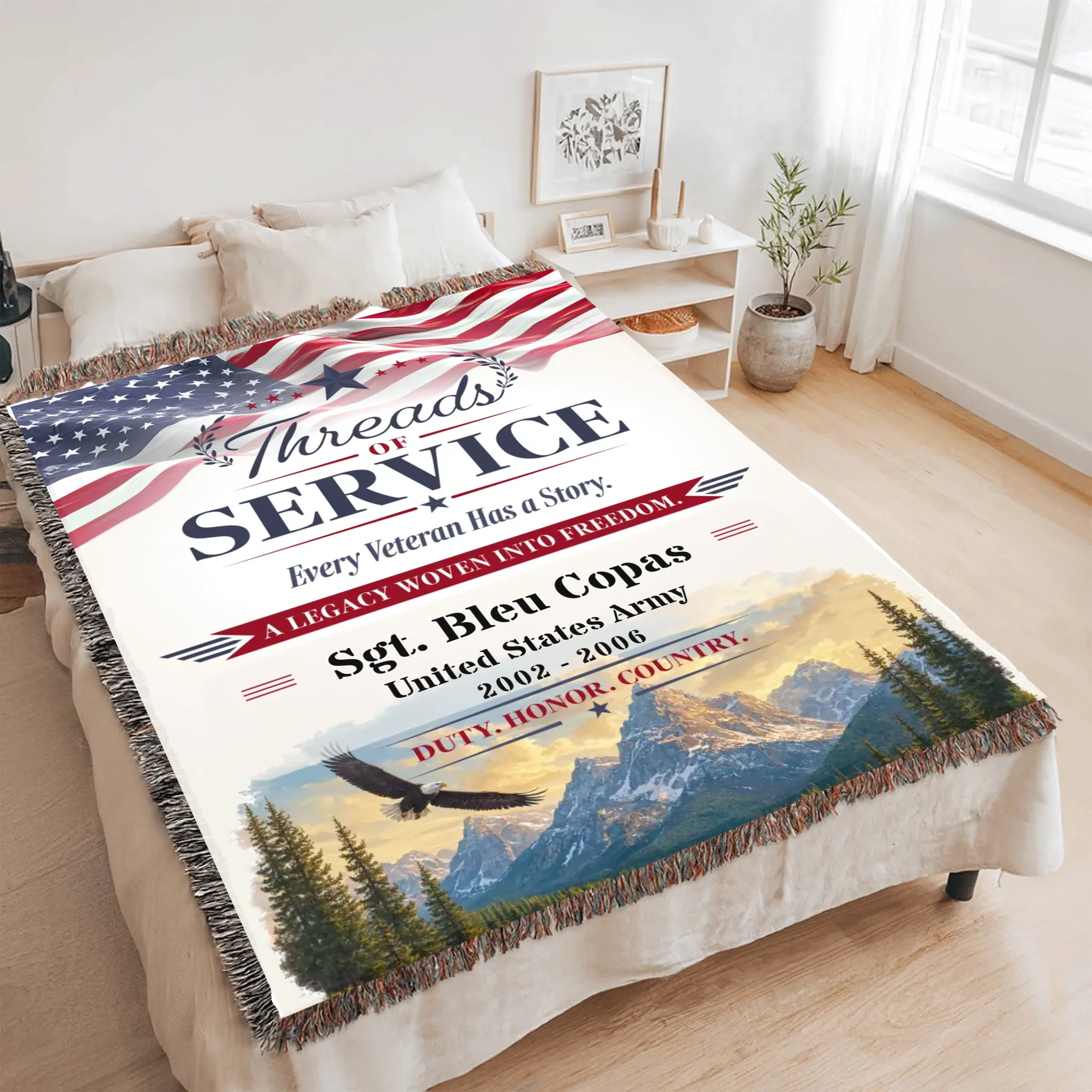 A veteran-themed throw blanket with fringe is displayed on a bed in a bright, modern bedroom. The blanket features a patriotic design with the text 'Threads of Service', an American flag, and a scenic mountain landscape with a bald eagle.